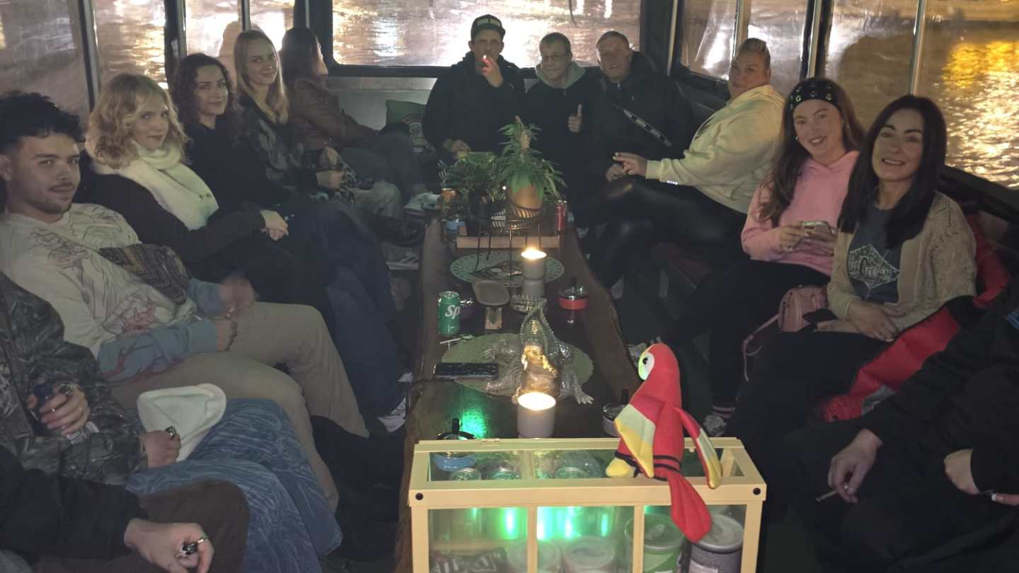 Group of people seated in a decorated boat with drinks and snacks on the table.