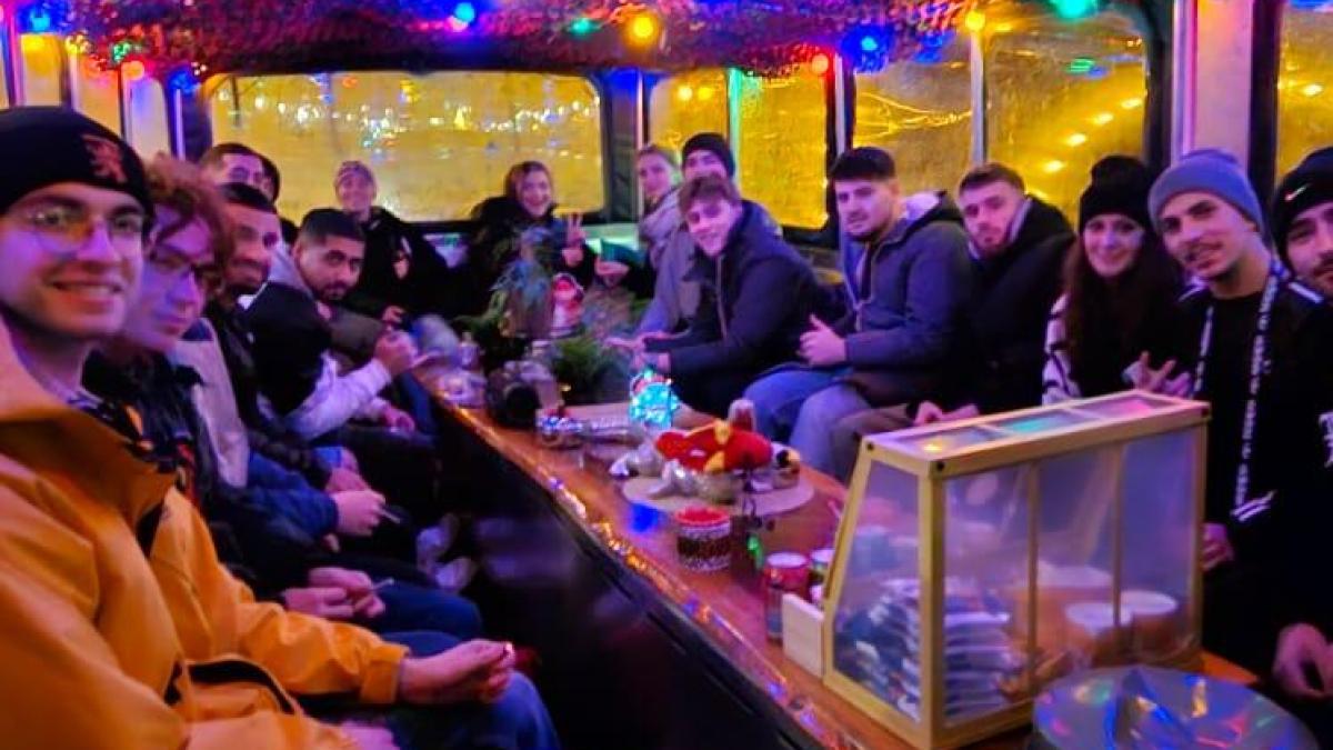 Group of people sitting at a table under colorful lights on a boat.