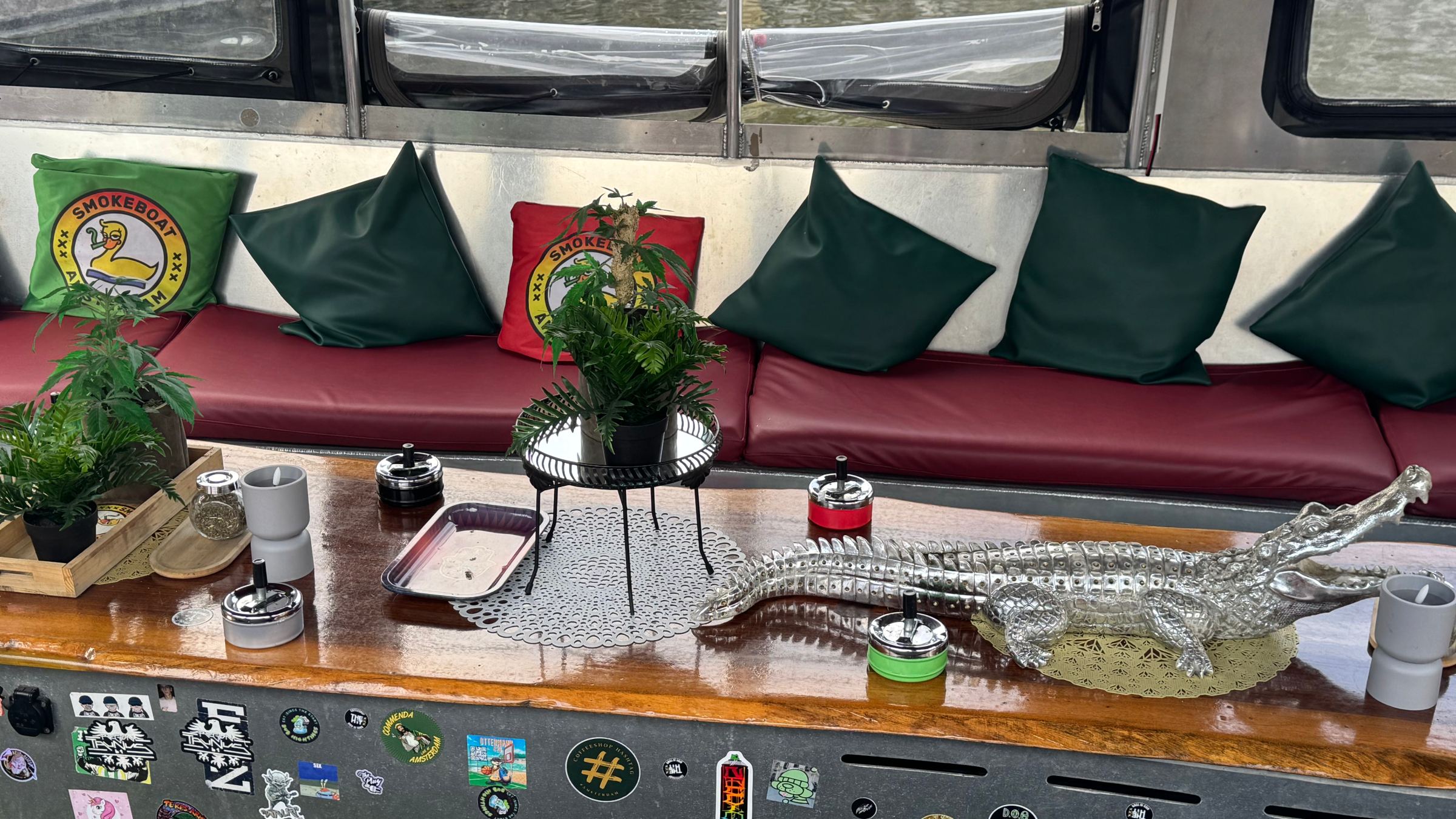 Bus interior with red seats, green pillows, plants, and a metal alligator on a decorated table.
