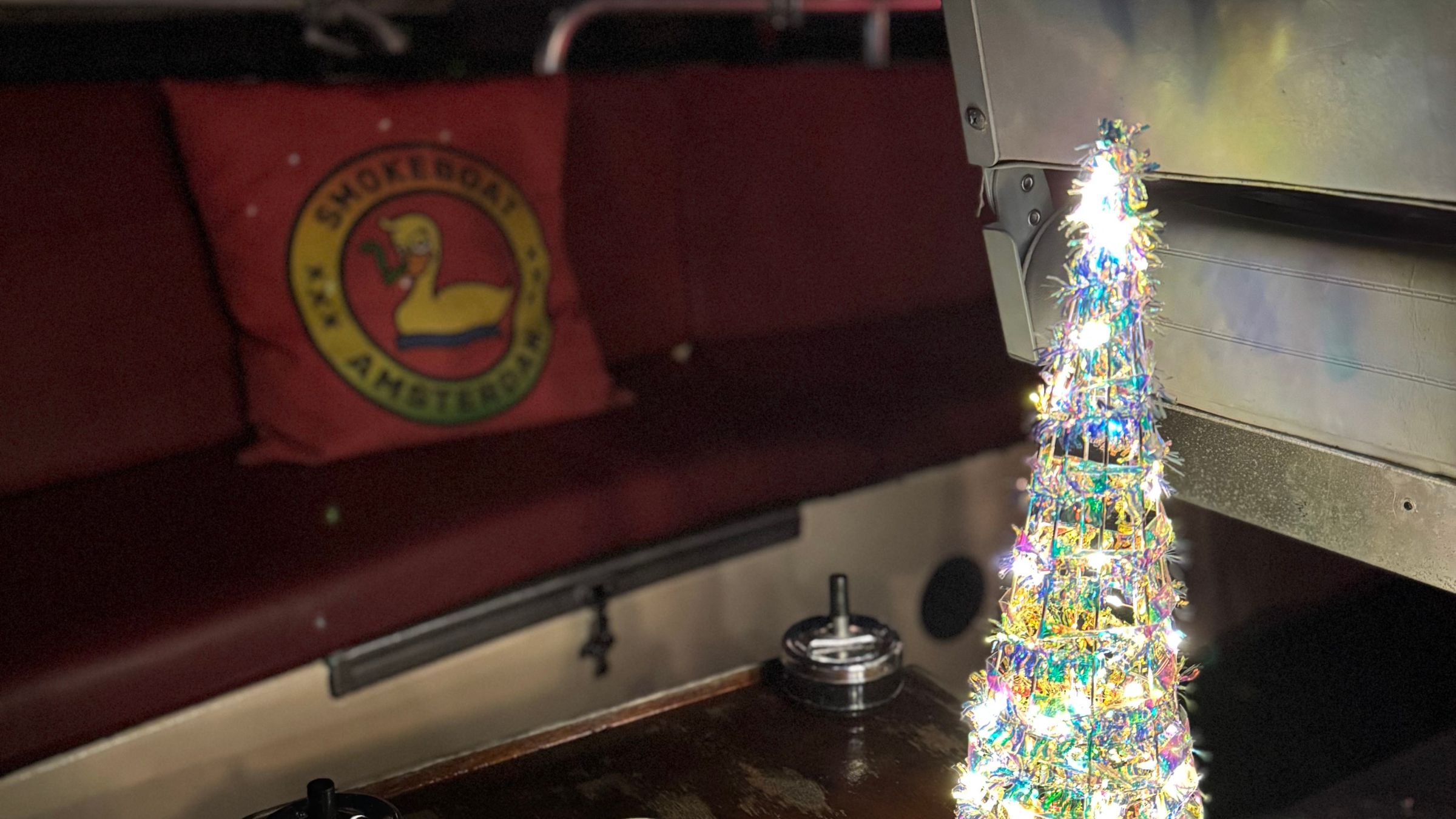 Small lit-up Christmas tree on a boat table with a red cushion.