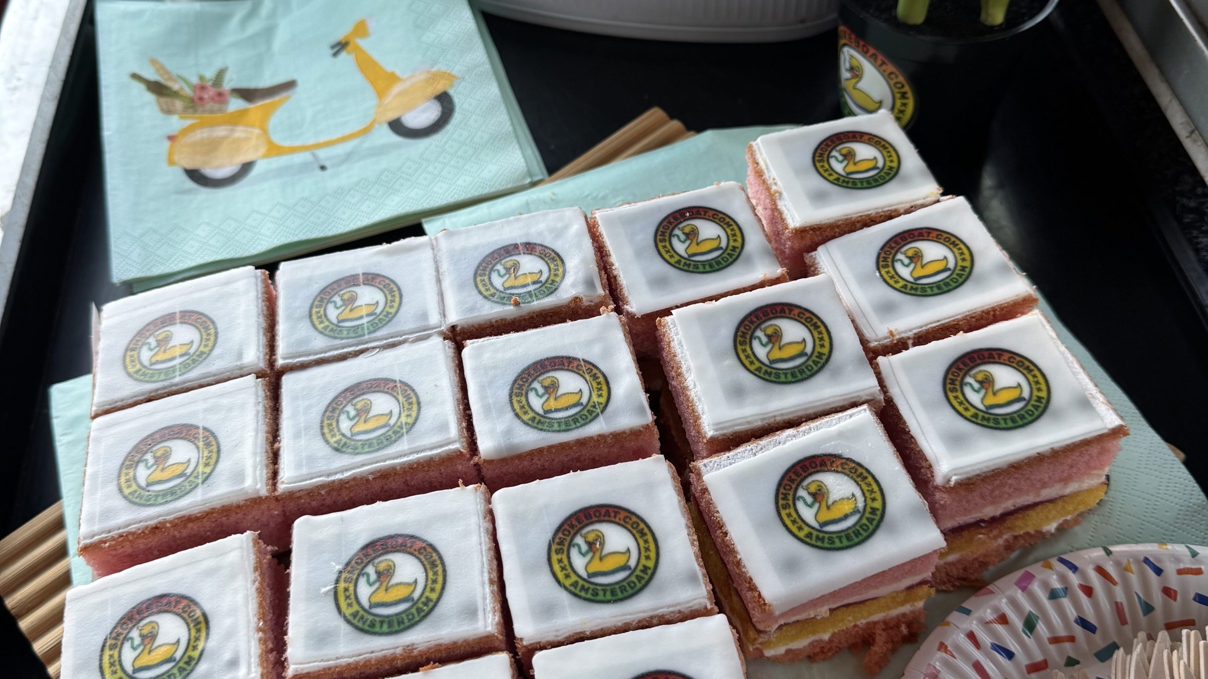 Square cakes with logo on top, tulips, and a white container.