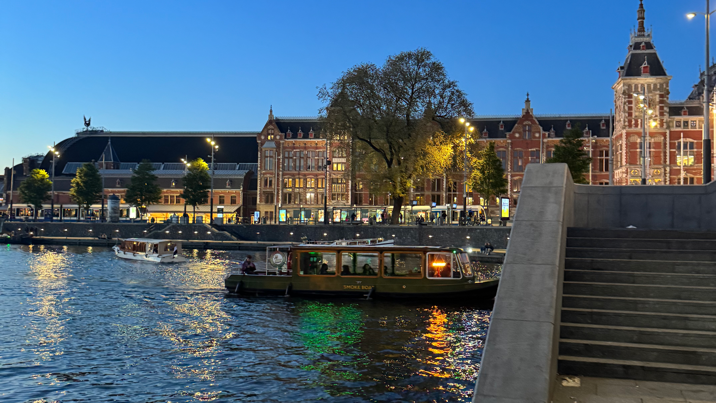 Evening view of a canal with boats and historic buildings along the waterfront under a clear blue sky.
