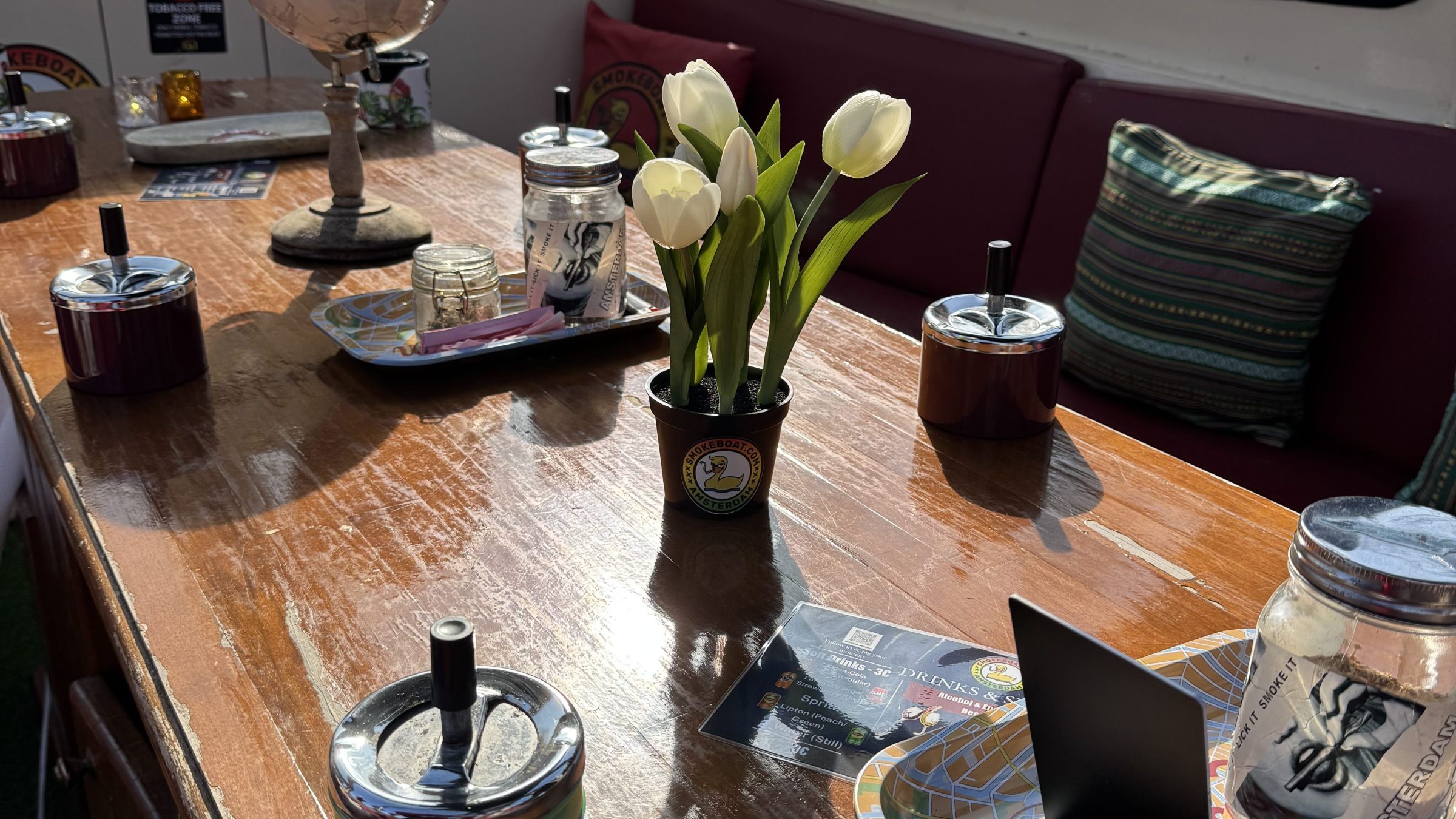 Wooden table with white tulips, a globe, jars, and a tablet inside a cozy space.