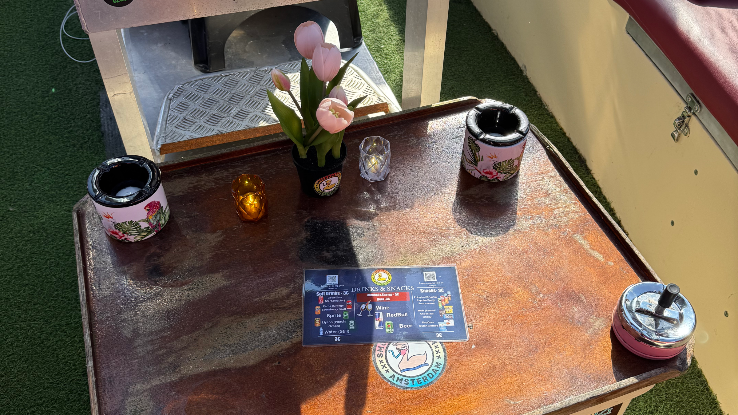 Outdoor seating with table, candles, flowers, coasters, stickers, and menu.