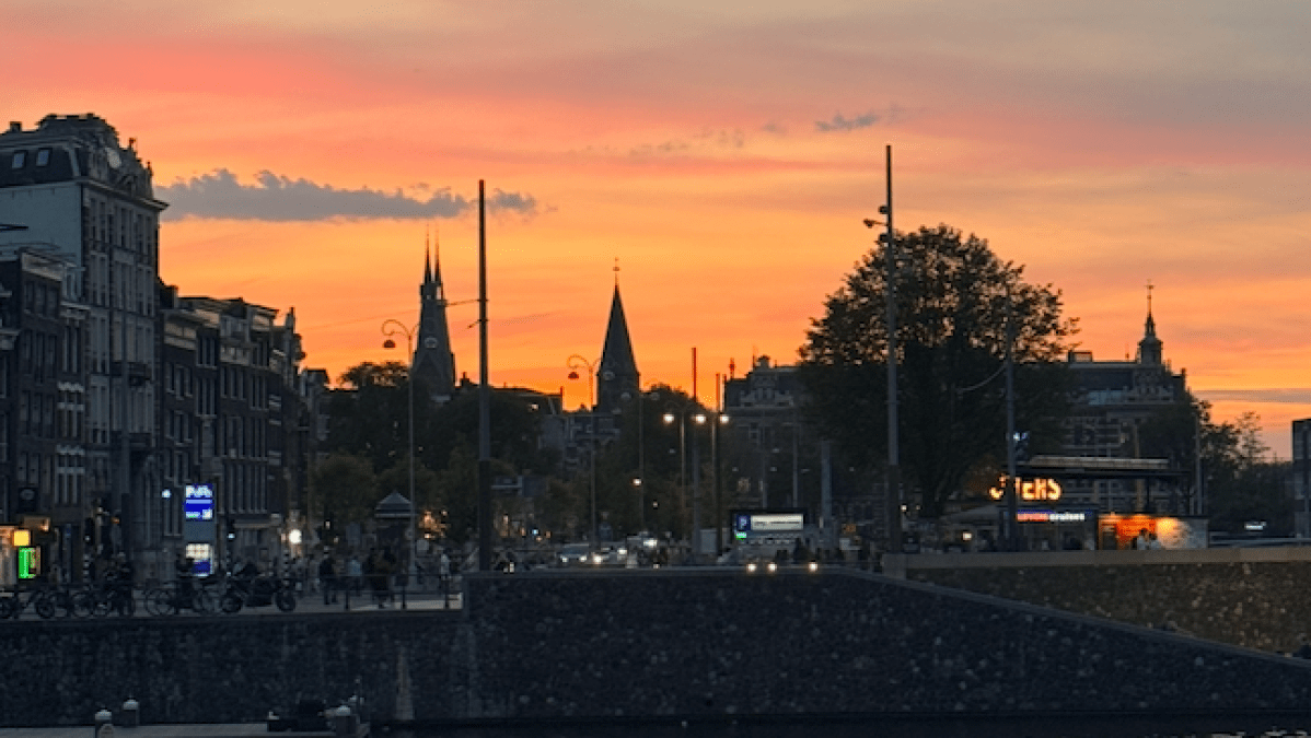 Boat on canal at sunset with city skyline and colorful sky.