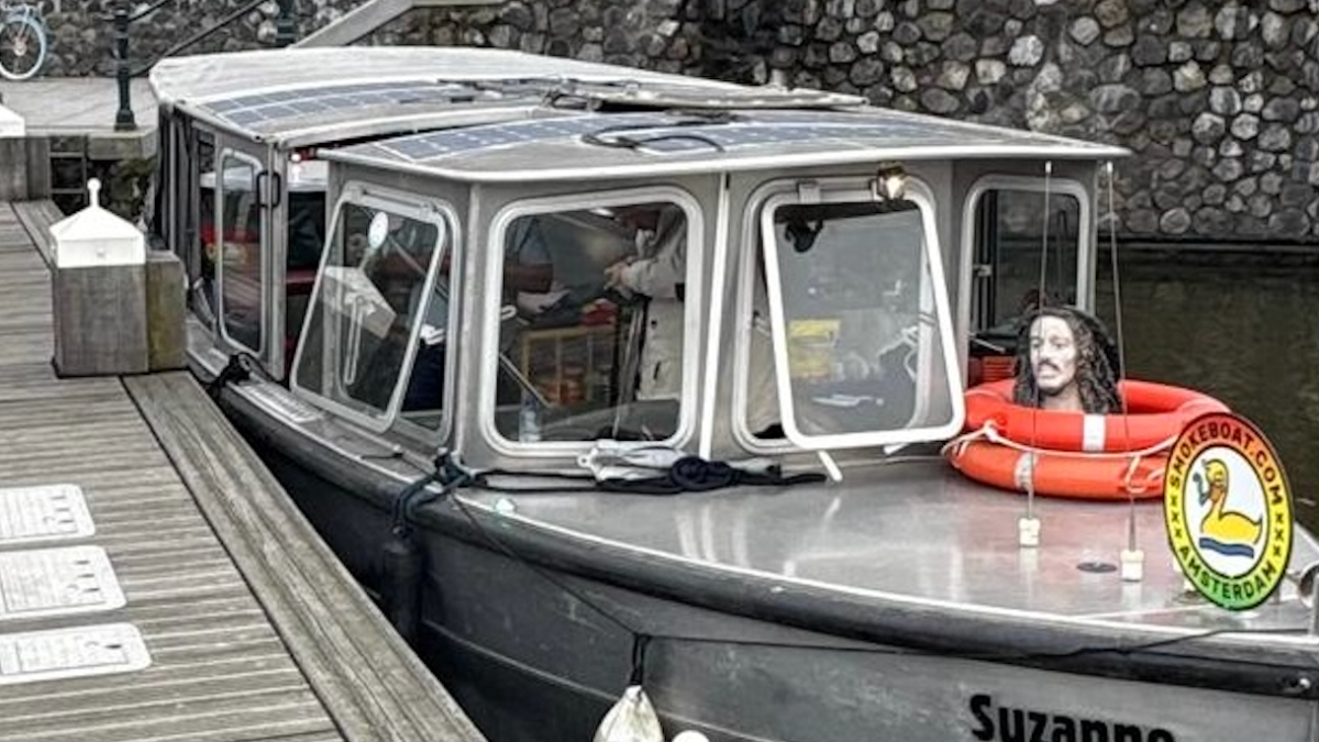 Small boat named Suzanne docked by a stone wall with people nearby.