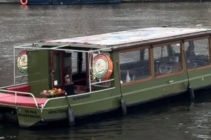 Green canal boat with glass roof on a calm river in Amsterdam.