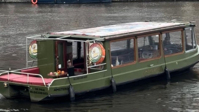 Green canal boat with glass roof on a calm river in Amsterdam.