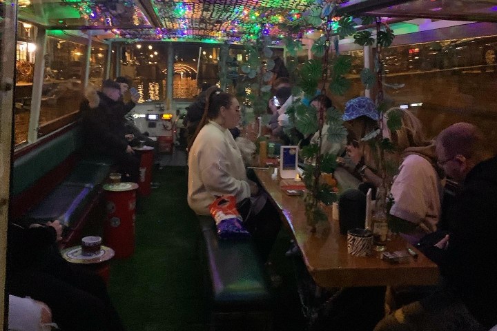 People in a colorful, decorated bus with lights, seated and talking.