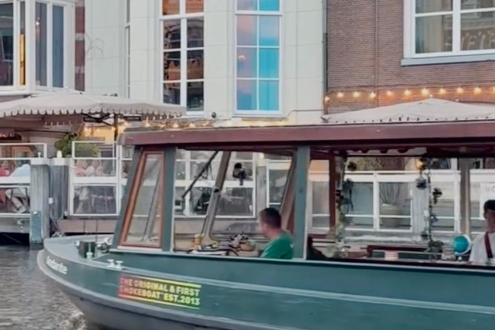 Small boat with people passing by a brick building along a canal.