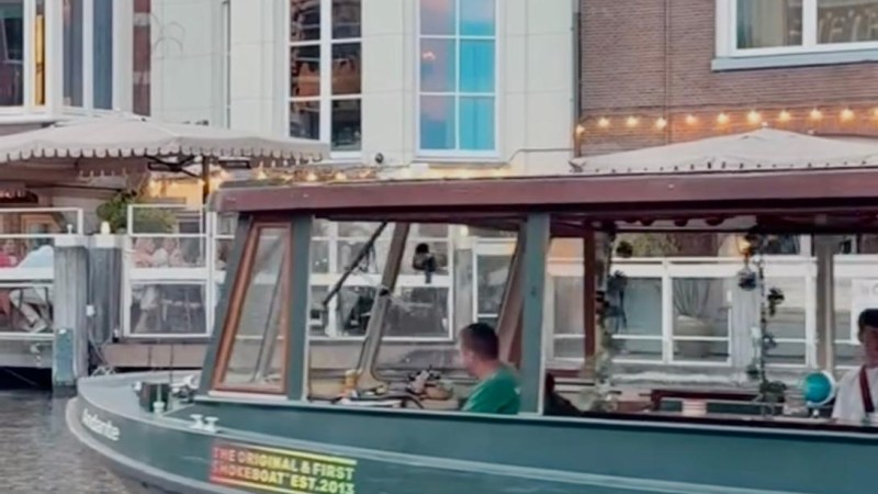 Small boat with people passing by a brick building along a canal.