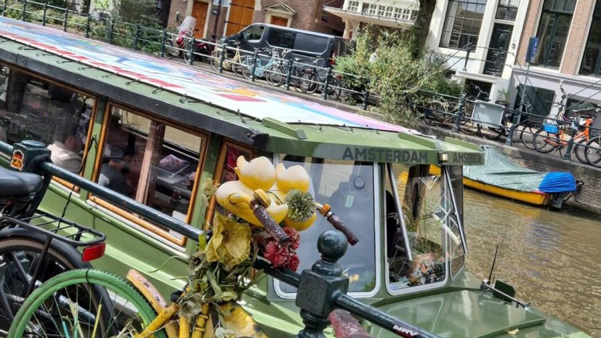 Decorated bike by canal with boat and historic buildings in Amsterdam.