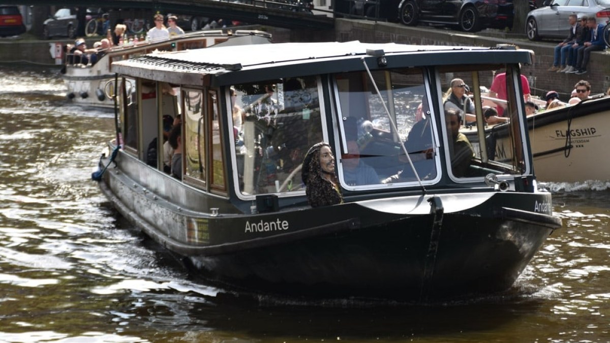 Boat named Andante cruising on a canal with historic buildings in the background.