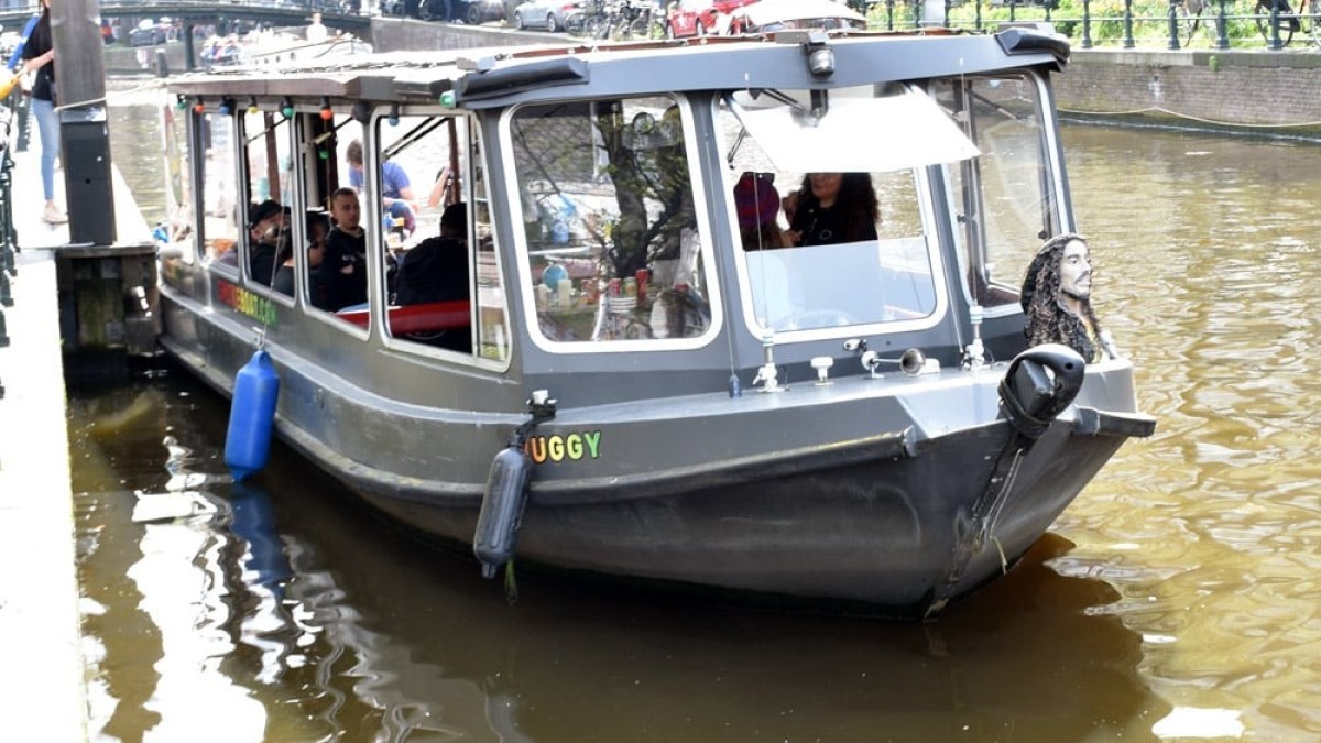 Tourist boat on a sunny canal lined with trees and buildings.